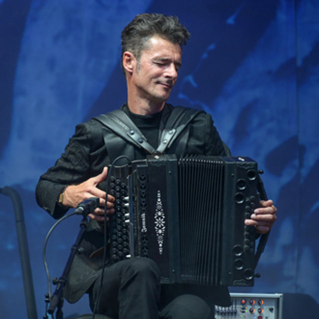 Herbert Pixner spielt auf der Bühne ein schwarzes Akkordeon, im Hintergrund ist blaues Licht zu sehen.
