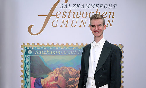 Dirigent Achleitner in schwarzem Frack und weißer Fliege steht vor Banner mit Schrift 'Salzkammergut Festwochen Gmunden'