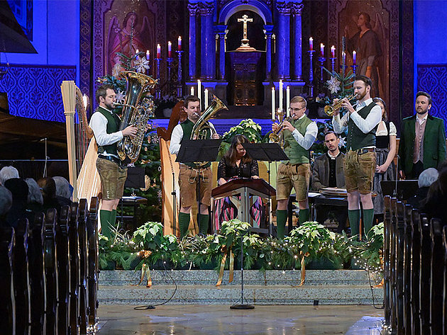 Das Salzkammergut Bläserquartett spielt in traditioneller Tracht vor einem Altar mit Kerzen und Kreuz in der festlich geschmückten Stadtpfarrkirche St. Nikolaus Bad Ischl, umgeben von Weihnachtsdekoration.