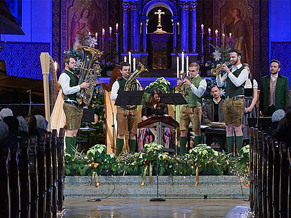 Das Salzkammergut Bläserquartett spielt in traditioneller Tracht vor einem Altar mit Kerzen und Kreuz in der festlich geschmückten Stadtpfarrkirche St. Nikolaus Bad Ischl, umgeben von Weihnachtsdekoration.
