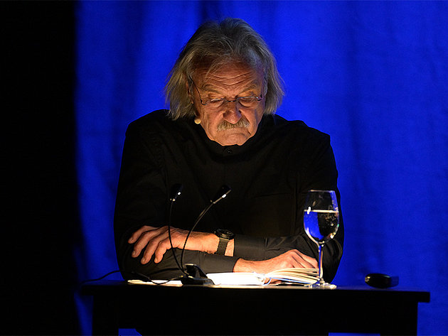 Christoph Ransmayr sitzt am Tisch auf der Bühne des Stadttheaters Gmunden während einer Lesung bei den Salzkammergut Festwochen am 25.05.2025, mit einem Glas Wasser und Mikrofon vor sich