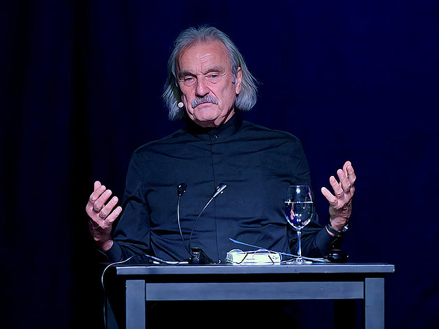 Christoph Ransmayr sitzt am Tisch auf der Bühne des Stadttheaters Gmunden während einer Lesung bei den Salzkammergut Festwochen am 25.05.2025, mit einem Glas Wasser und Mikrofon vor sich
