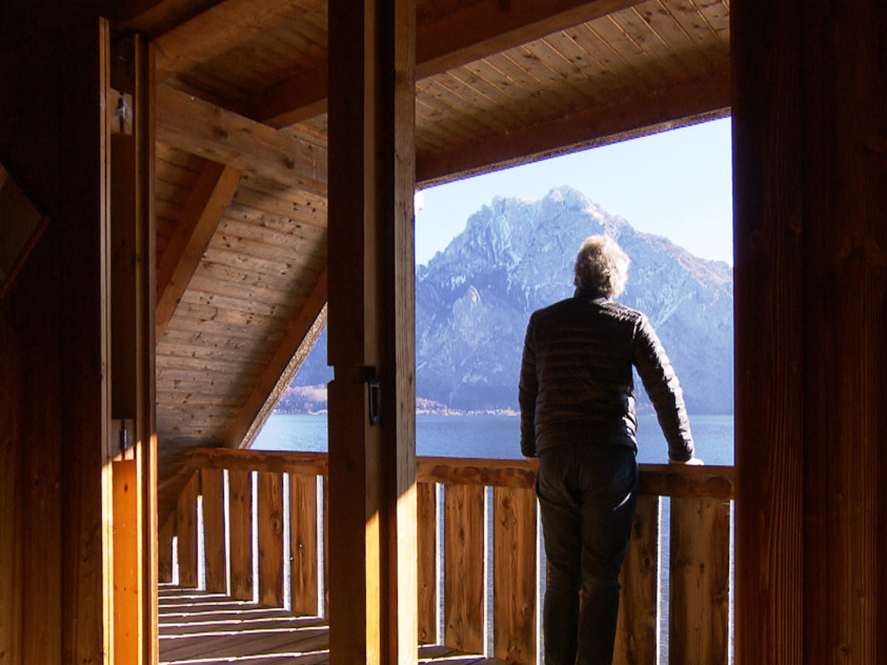  Franz Welser-Moest steht auf einem Holzbalkon und blickt auf  Traunsee und dem sonnenbeschienenen Traunstein in der Ferne.