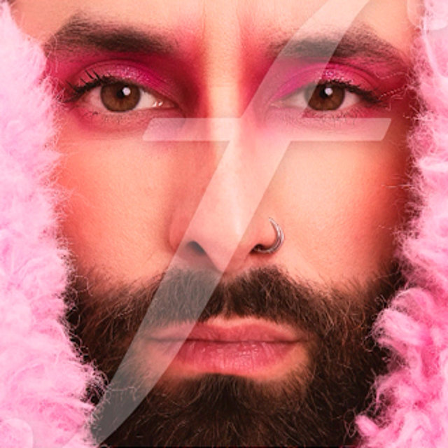 Eine Person mit Vollbart, rosa Augen-Make-up und einer rosa Kapuze blickt direkt in die Kamera.